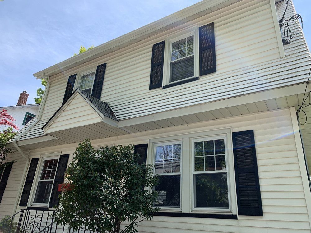 Two-story white house with black shutters, windows, and light blue sky.