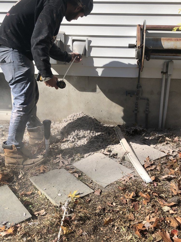 Man using a power tool outside; dust and debris near a wall and stepping stones.