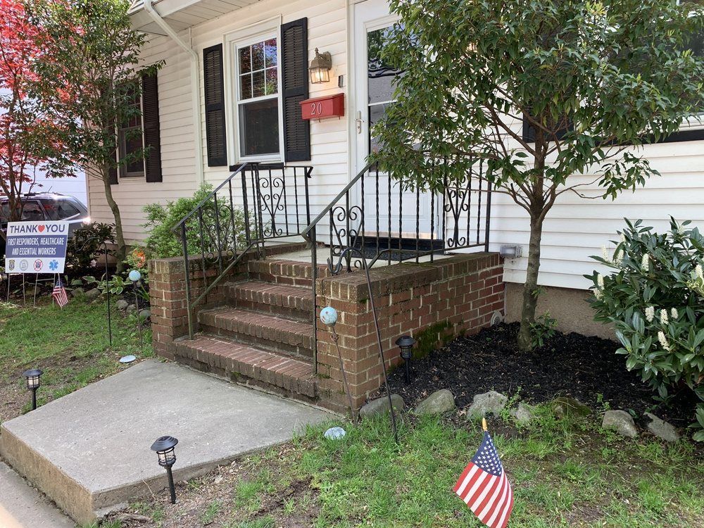 Brick steps leading to a white house with black railing. American flag and small trees in the yard.