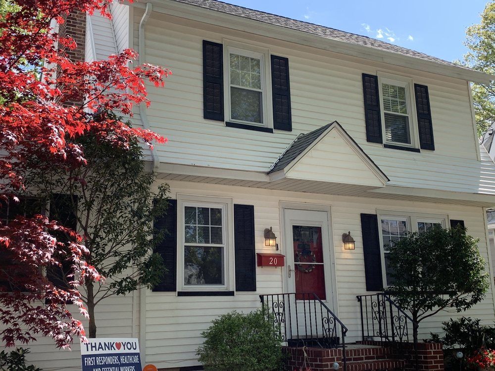 Two-story white house with black shutters, red door, and small front porch.