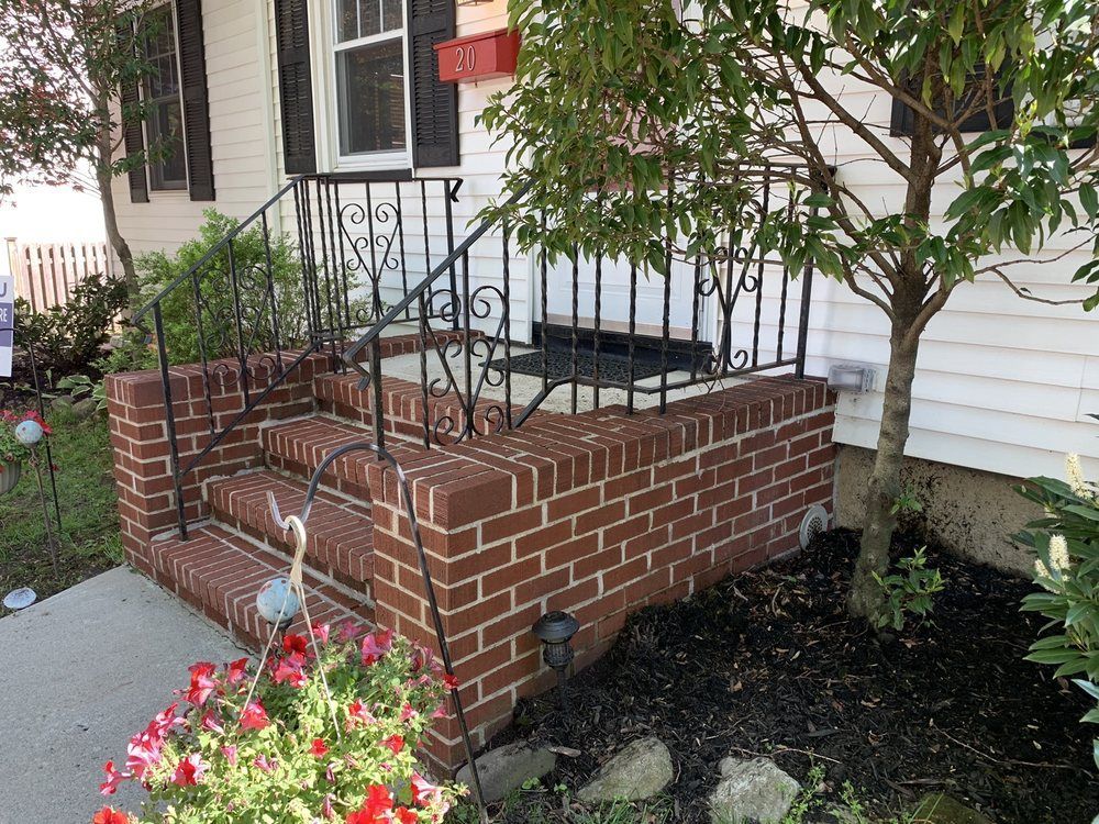 Brick front porch with black railing and steps leading to a white house.