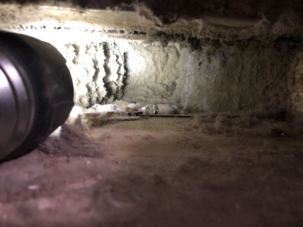Dust-filled vent interior, illuminated by a flashlight. Thick debris covers walls and bottom surface.