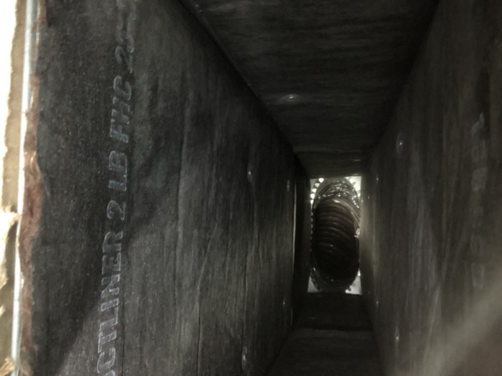 Interior view of a rectangular HVAC duct lined with dark material, with a circular object visible at the end.