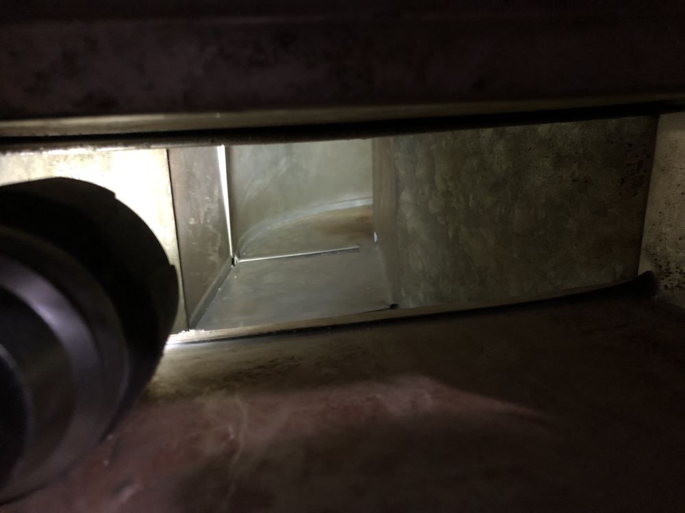 Interior view of a duct system, with a rectangular opening and dark, metal walls.