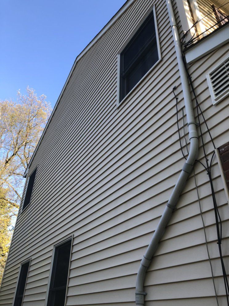Beige siding on a two-story house with a white downspout and windows; blue sky background.