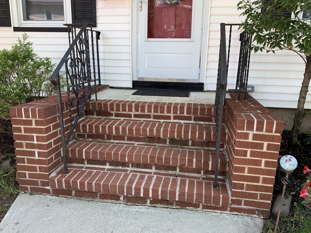 Brick steps leading to a white door. Black wrought-iron railings. Red brick walls and steps.