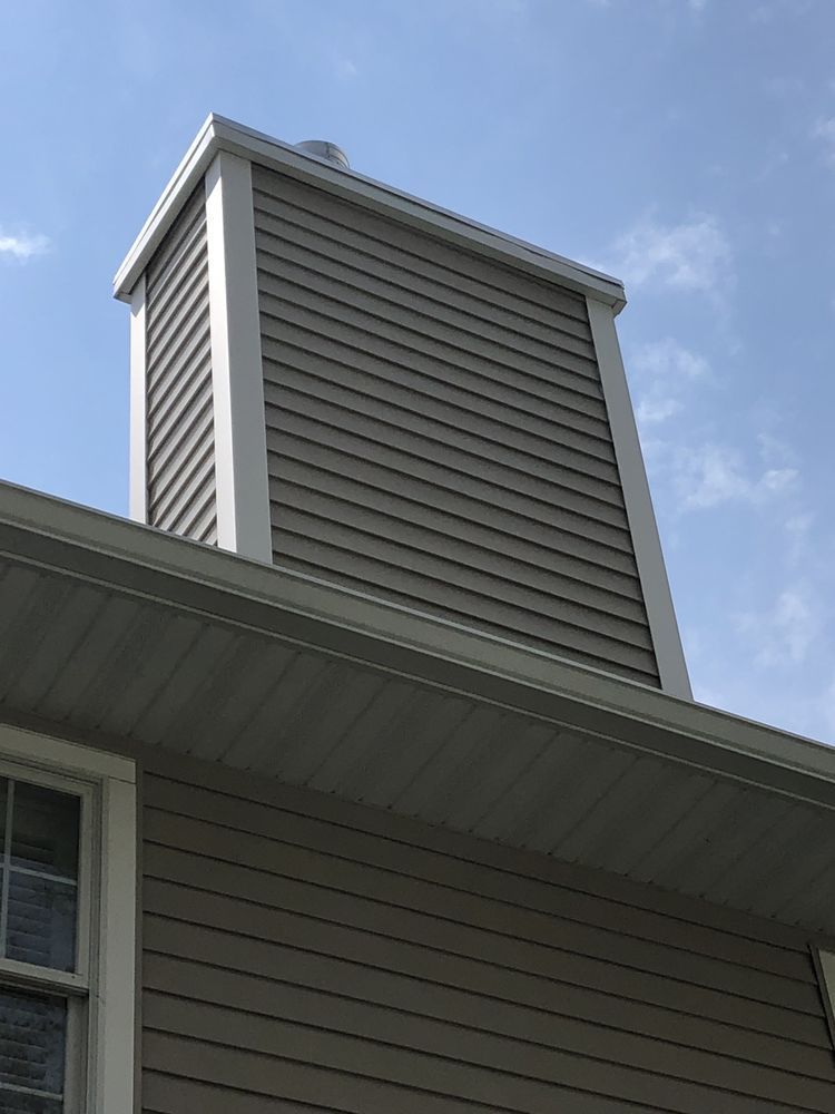 Chimney with gray siding and white trim against a blue sky.