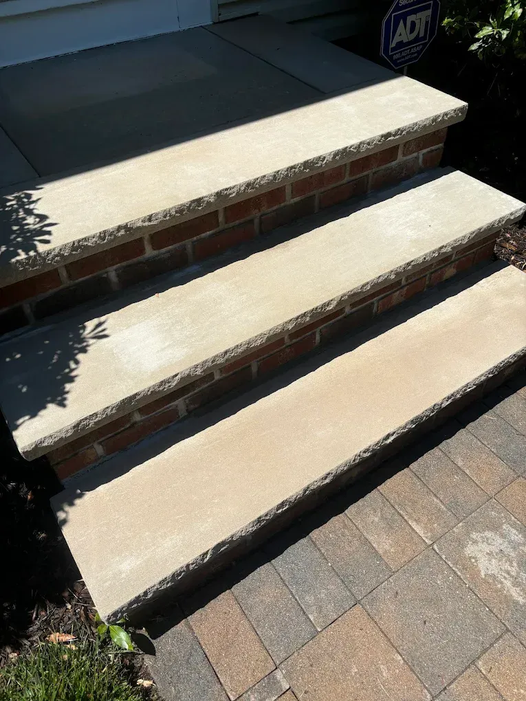 Three concrete steps with brick risers leading to a front door.