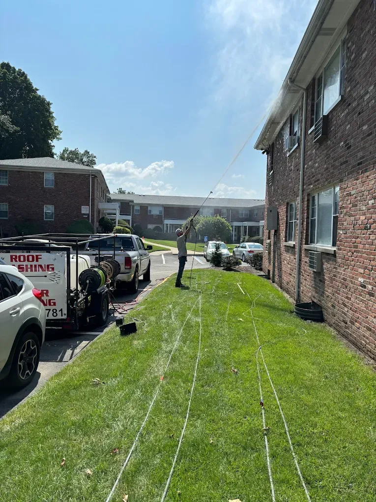 Man washing exterior of building with equipment on grassy area, sunny day.