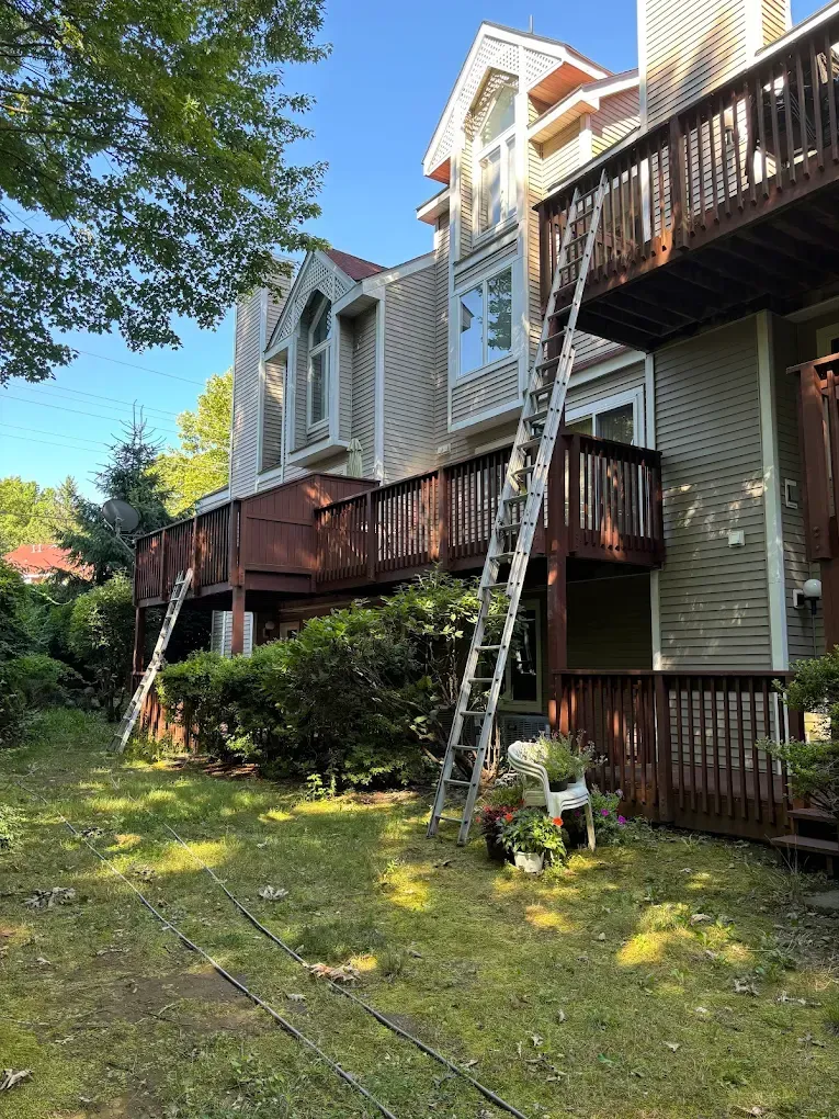 Two ladders propped against a multi-story building with decks; the exterior is light brown.
