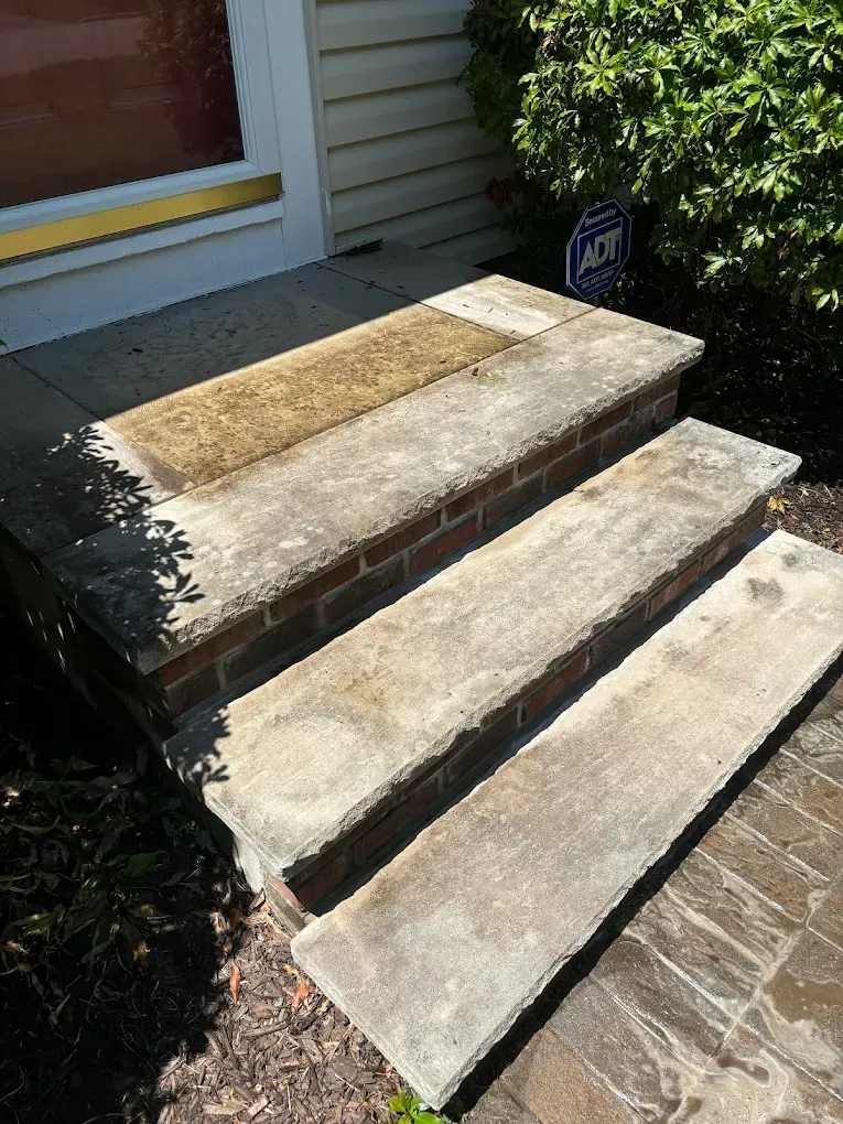 Brick and concrete steps leading up to a house entrance. The steps are weathered, and stained, with a brown area on top.