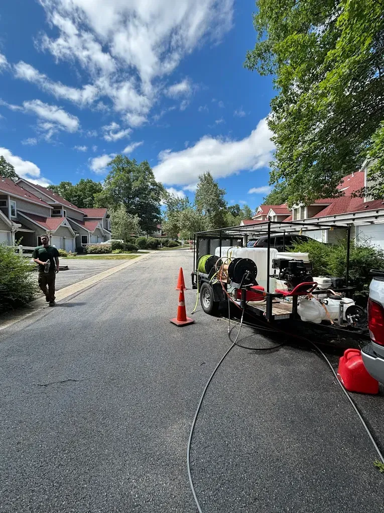 A person walking on a road near a pressure washing setup; houses and trees under a blue, cloudy sky.