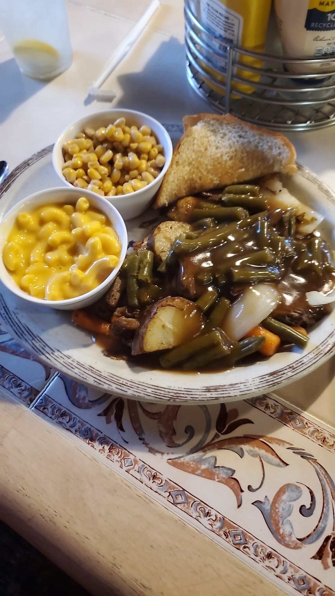 A plate of food with green beans , macaroni and cheese , corn and toast on a table.