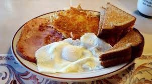 A plate of food with eggs , ham , hash browns and toast on a table.