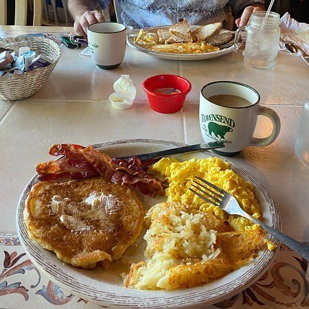 A plate of food with pancakes , eggs , bacon and hash browns on a table.