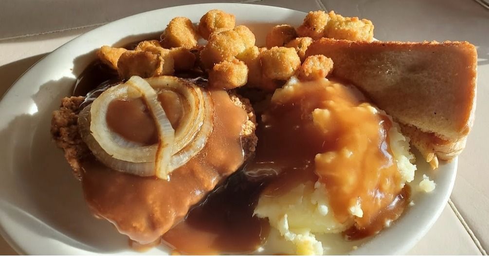 A white plate topped with meat , mashed potatoes , gravy , onions and bread.