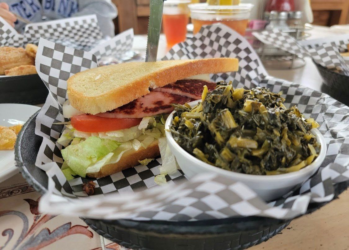 A sandwich and a bowl of greens in a basket on a table