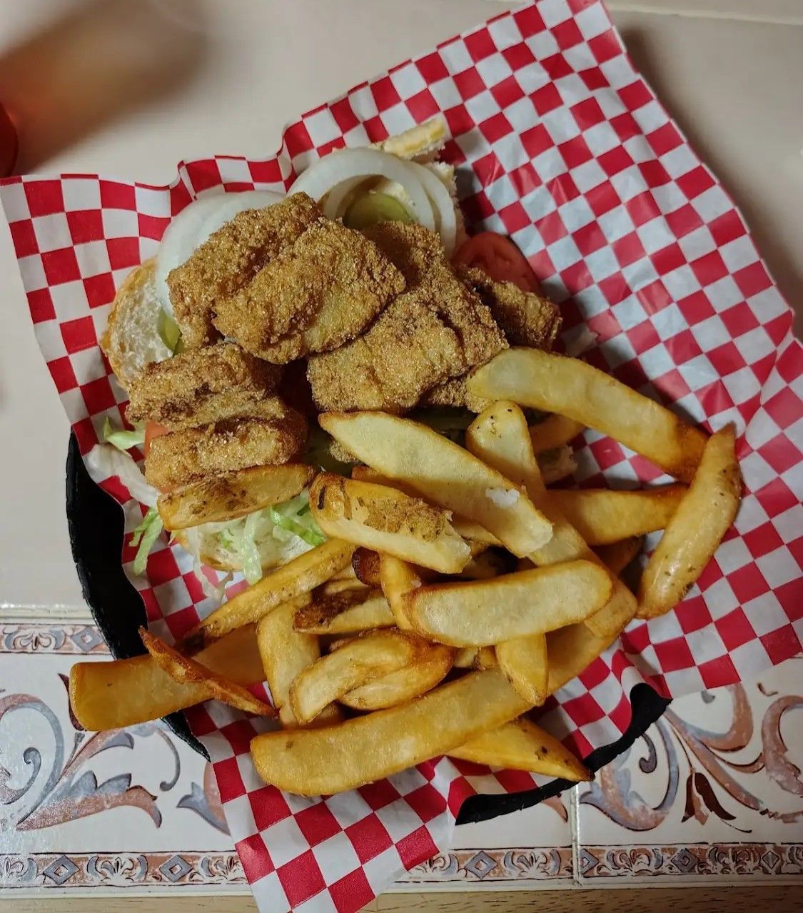 A fried chicken sandwich with french fries on a checkered paper