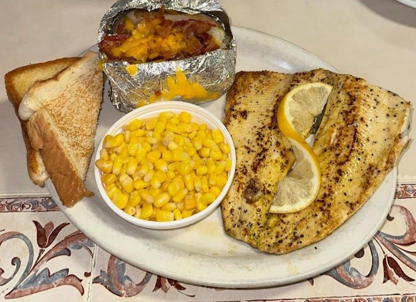 A white plate topped with fish , corn and a baked potato.