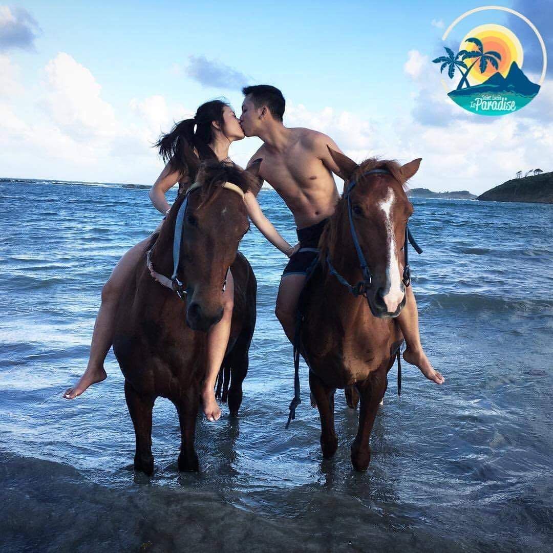 A man and a woman are kissing while riding horses on the beach