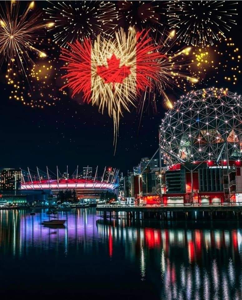 A fireworks display over a city at night with a maple leaf in the middle.
