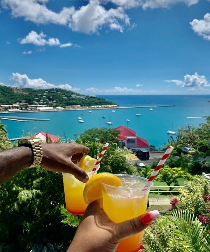 A person is holding two drinks with straws in front of a body of water.