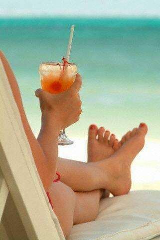 A woman is sitting on a beach holding a drink in her hand.