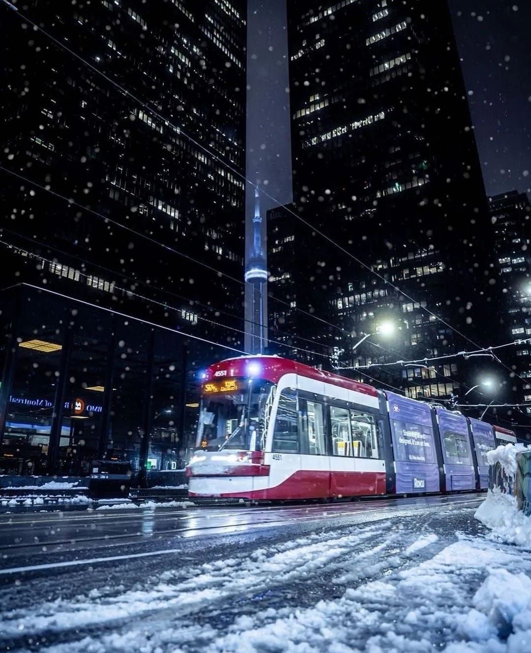 A red and white bus is driving down a snowy city street at night.