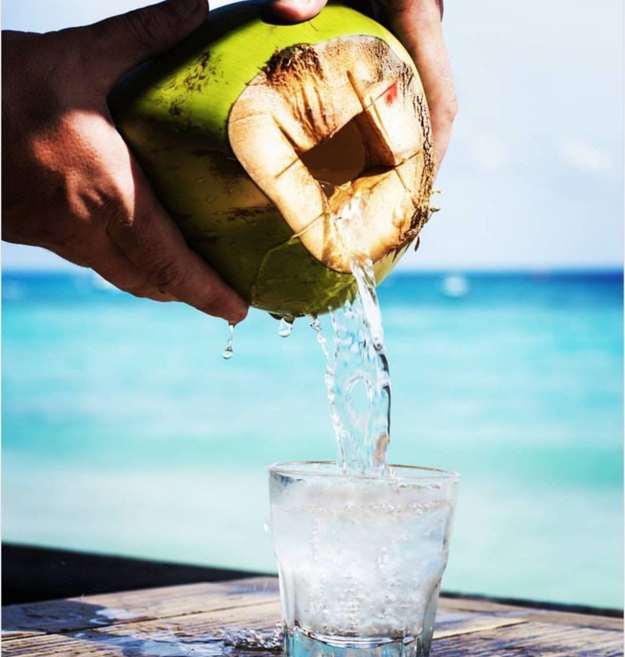 A person is pouring water from a coconut into a glass