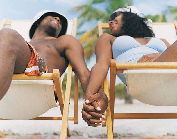 A man and a woman are holding hands while laying in beach chairs