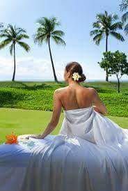 A woman is sitting on a massage table with palm trees in the background.