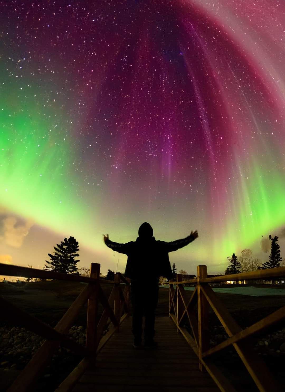 A person is standing on a bridge looking at the aurora borealis