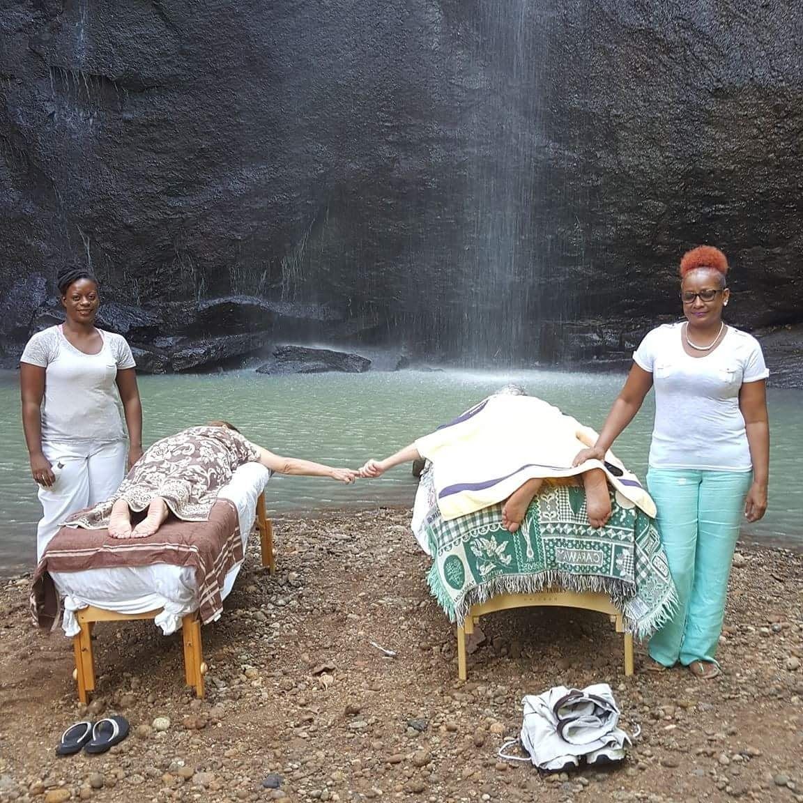 Two women standing next to a waterfall with a person laying on a bed that says okay