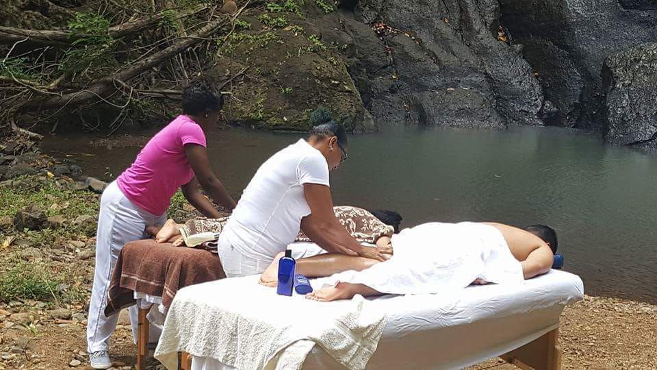 Two women are giving a man a massage in front of a waterfall