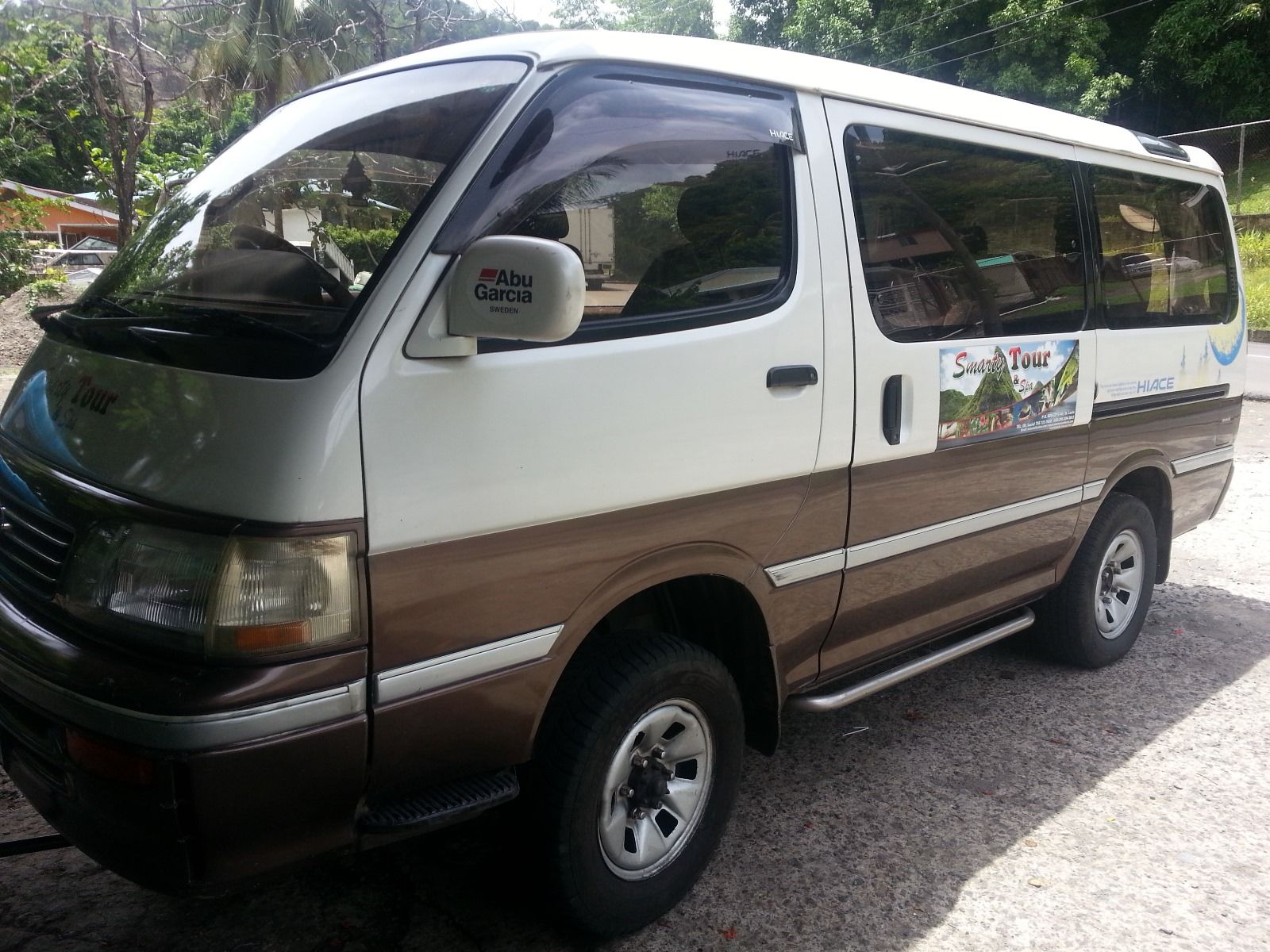 A white and brown van is parked on a gravel road.