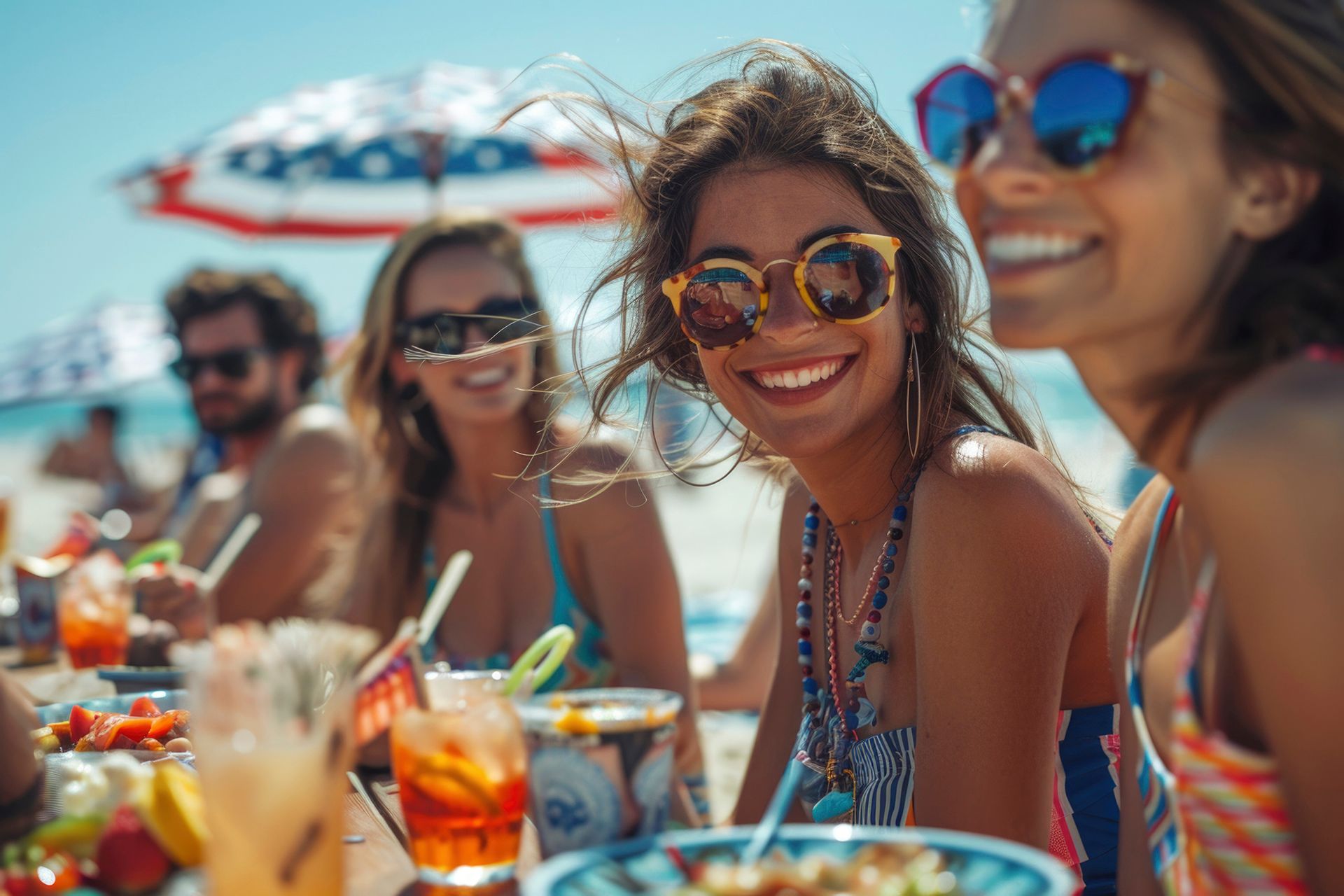 A group of women are sitting at a table on the beach eating and drinking.