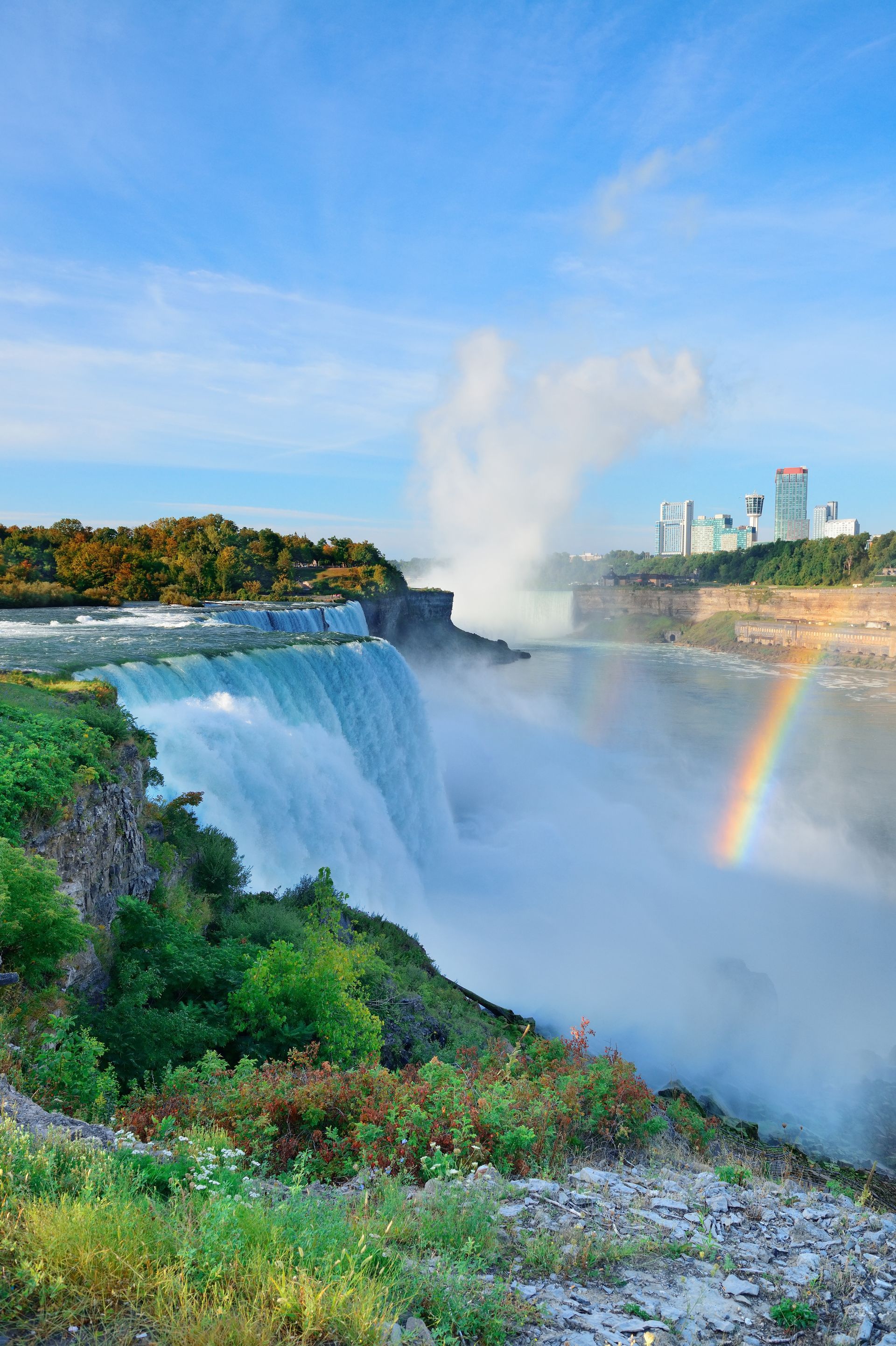 A waterfall with a rainbow in the background and a city in the background.