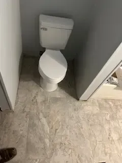 A toilet is sitting in a corner of a bathroom next to a door.