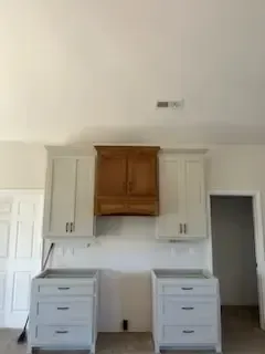 A kitchen with white cabinets and a wooden hood.