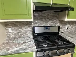 A stove top oven is sitting in a kitchen with green cabinets.