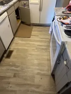 A kitchen with a wooden floor , white cabinets , a stove and a refrigerator.