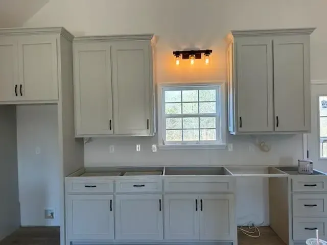 A kitchen with white cabinets , a sink , and a window.