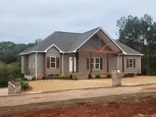 A large house is sitting on top of a dirt road surrounded by trees.