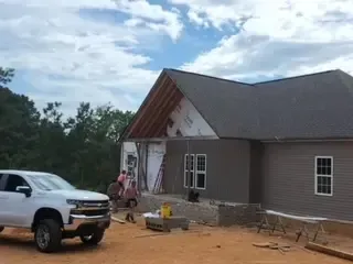 A white truck is parked in front of a house under construction.
