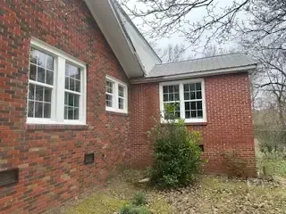 A brick house with two windows and a bush in front of it.