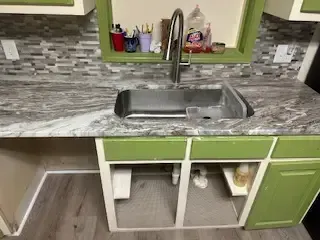 A kitchen sink with a faucet and green cabinets.
