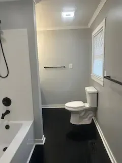 A bathroom with a toilet , tub , shower and window.