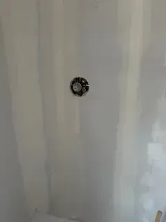 A white wall with a hole in it and a clock on it.