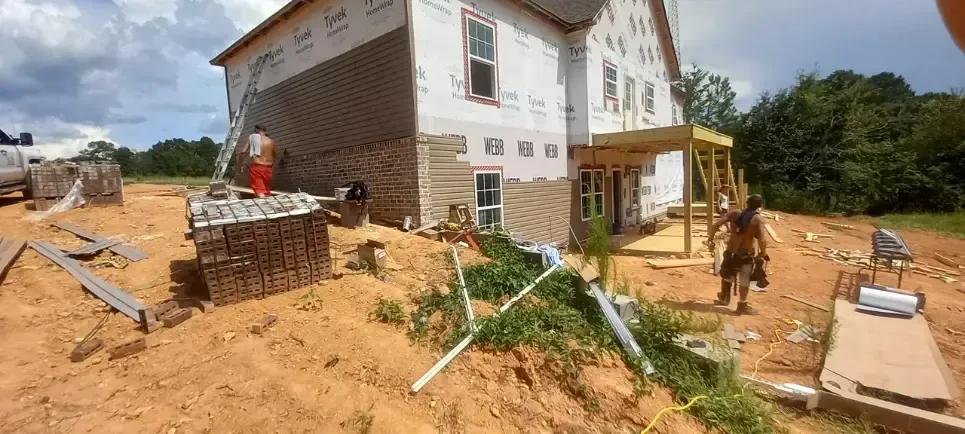 A large white house is being built in a dirt field.
