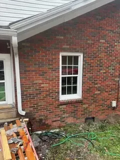 A brick house with a white window and a hose in front of it.
